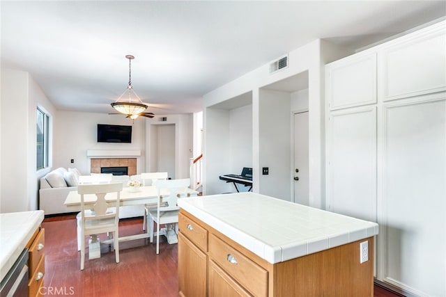 kitchen with tile counters, a tile fireplace, hanging light fixtures, a kitchen island, and dark hardwood / wood-style flooring