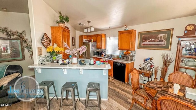 kitchen featuring kitchen peninsula, decorative light fixtures, light hardwood / wood-style flooring, stainless steel appliances, and a kitchen breakfast bar