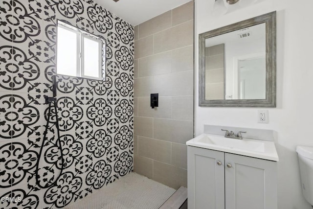 bathroom featuring toilet, vanity, and tiled shower