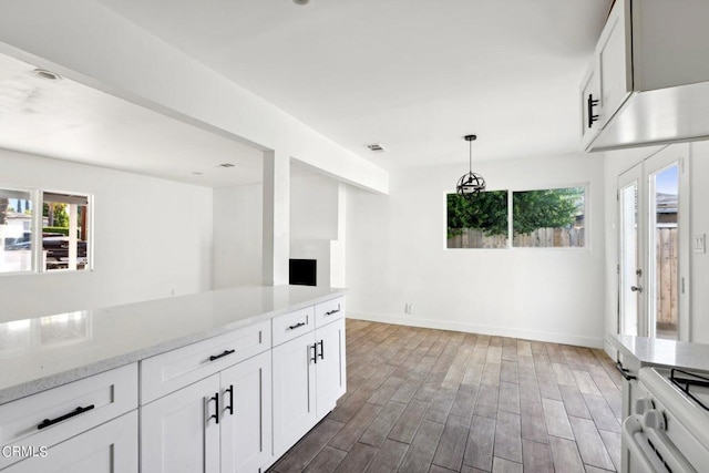 kitchen with decorative light fixtures, stove, white cabinetry, light stone counters, and dark hardwood / wood-style flooring