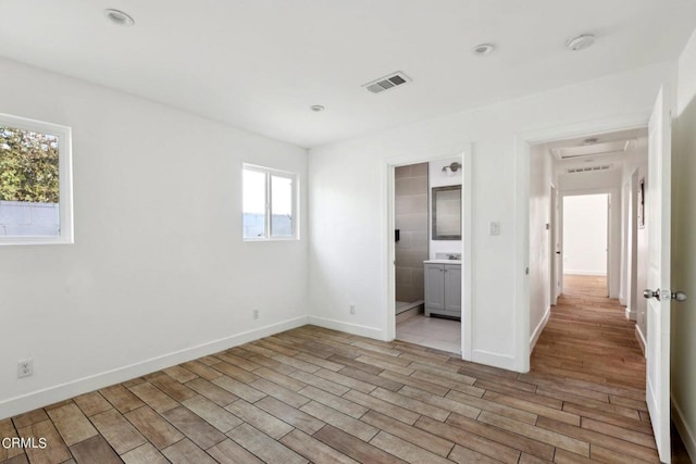 unfurnished bedroom featuring ensuite bath and light wood-type flooring