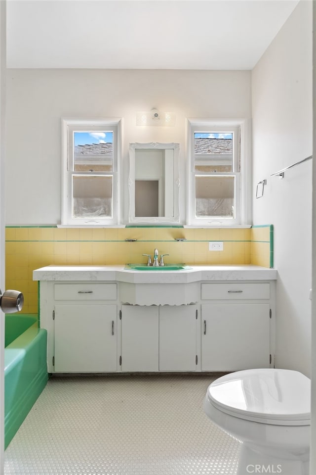 bathroom featuring tile walls, vanity, tile patterned flooring, toilet, and a washtub