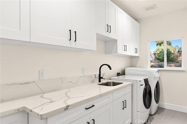 clothes washing area with cabinets, washing machine and dryer, light tile patterned flooring, and sink