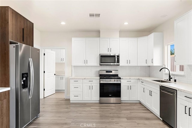 kitchen with sink, white cabinets, stainless steel appliances, and light hardwood / wood-style floors