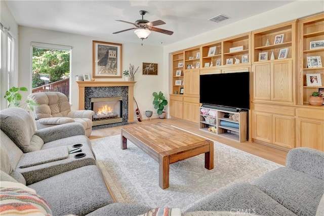 living room with visible vents, a fireplace with flush hearth, a ceiling fan, and light wood-style floors