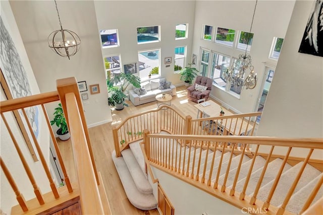 staircase featuring a chandelier, a high ceiling, baseboards, and wood finished floors