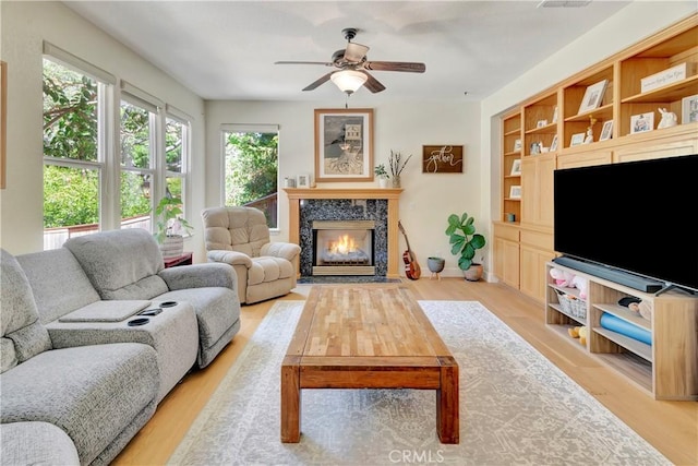 living room with built in features, a ceiling fan, light wood-style floors, and a high end fireplace