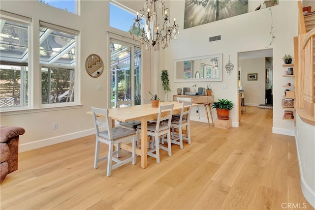 dining space featuring light wood-type flooring, baseboards, visible vents, and a towering ceiling