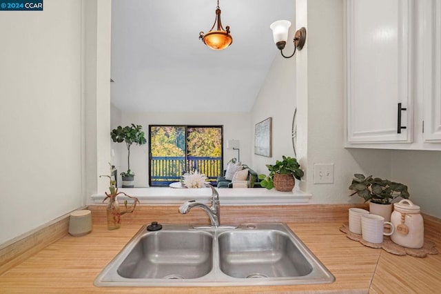 kitchen with lofted ceiling, white cabinetry, and sink