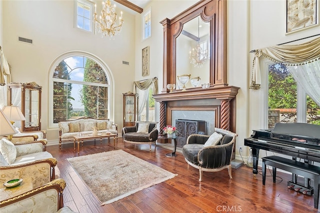 living area with a towering ceiling, dark wood-type flooring, a premium fireplace, and a notable chandelier