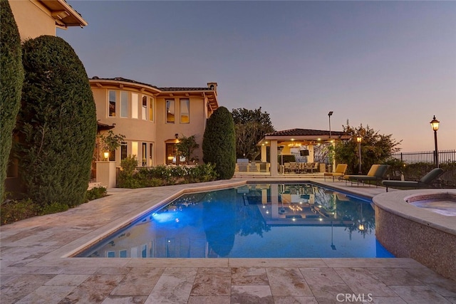 pool at dusk with an in ground hot tub and a patio