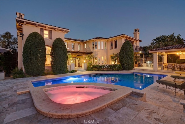 pool at dusk featuring a patio and an in ground hot tub