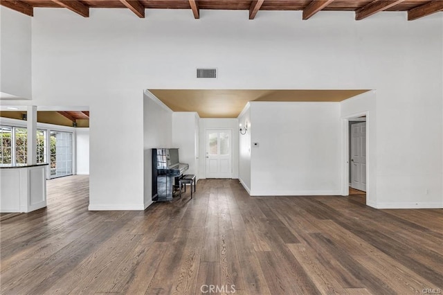 unfurnished living room featuring dark wood-type flooring, beam ceiling, and a towering ceiling