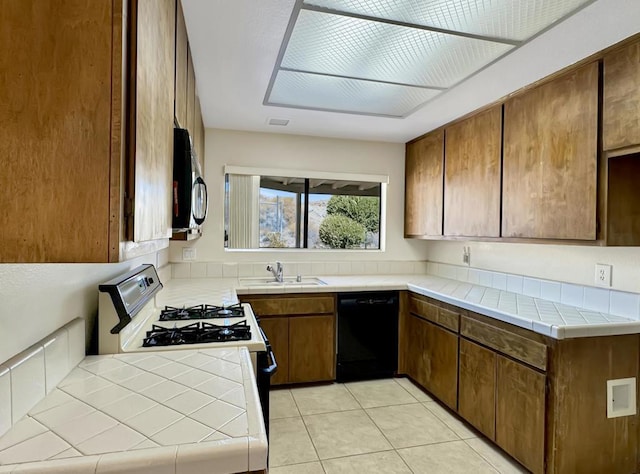 kitchen featuring white gas stove, sink, light tile patterned floors, black dishwasher, and tile counters