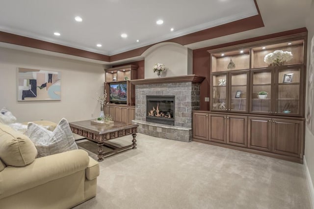 living room featuring light carpet, a stone fireplace, ornamental molding, and a tray ceiling