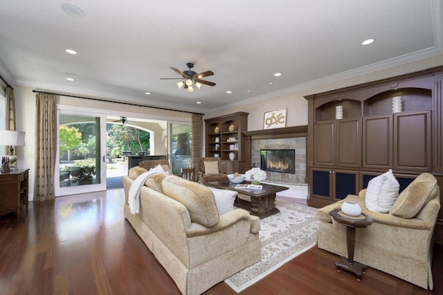 living room with ornamental molding, dark wood-type flooring, a tiled fireplace, and ceiling fan