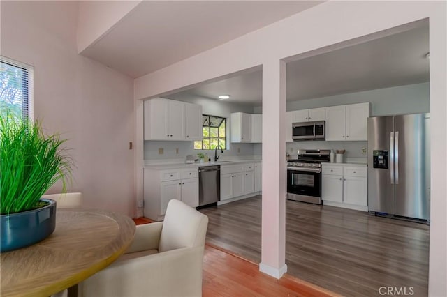 kitchen with appliances with stainless steel finishes, sink, white cabinetry, and hardwood / wood-style floors