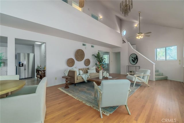 living room with light hardwood / wood-style floors, ceiling fan with notable chandelier, and high vaulted ceiling