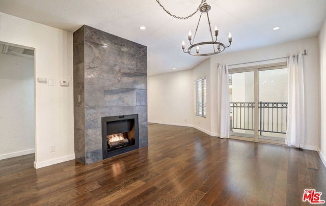 unfurnished living room with a notable chandelier, dark hardwood / wood-style floors, and a tiled fireplace