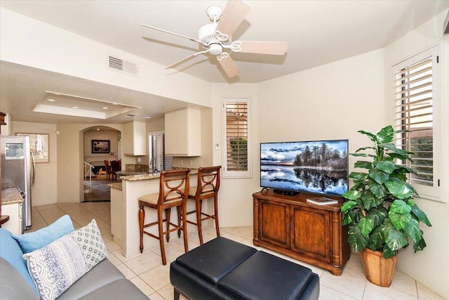 living room with ceiling fan, a raised ceiling, and light tile patterned floors