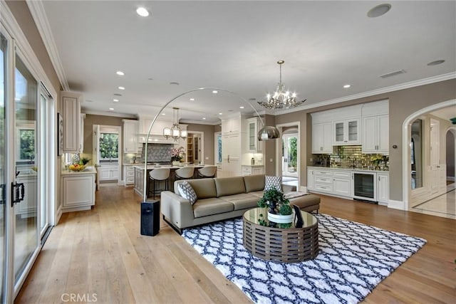 living room featuring ornamental molding, light hardwood / wood-style flooring, beverage cooler, and a healthy amount of sunlight