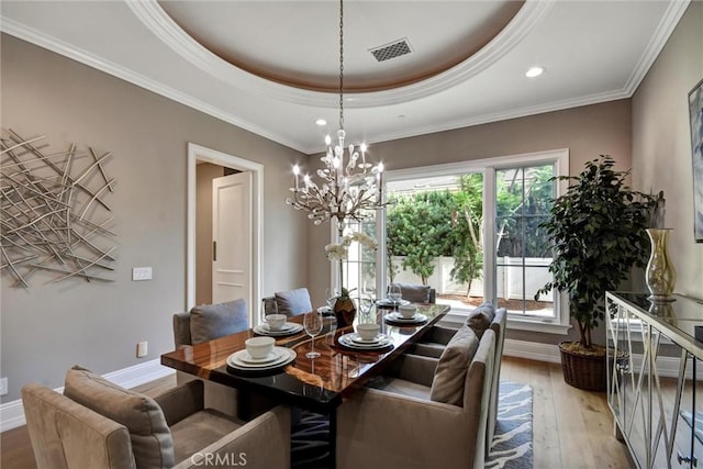 dining area with a chandelier, ornamental molding, light hardwood / wood-style floors, and a tray ceiling