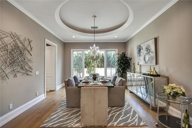 dining space featuring a tray ceiling, a chandelier, ornamental molding, and hardwood / wood-style flooring