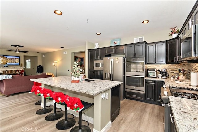 kitchen featuring light stone countertops, appliances with stainless steel finishes, sink, a center island with sink, and a breakfast bar area