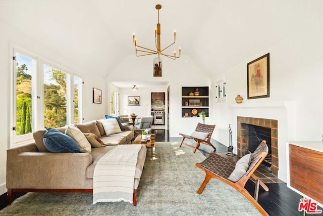 living room with high vaulted ceiling, a tiled fireplace, wood-type flooring, built in features, and a notable chandelier