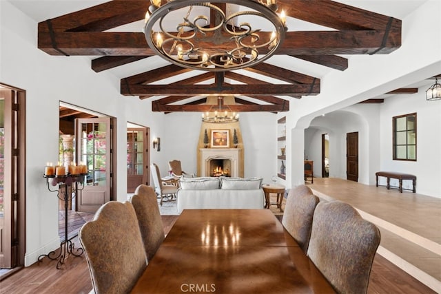 dining area with an inviting chandelier, vaulted ceiling with beams, a fireplace, and hardwood / wood-style floors