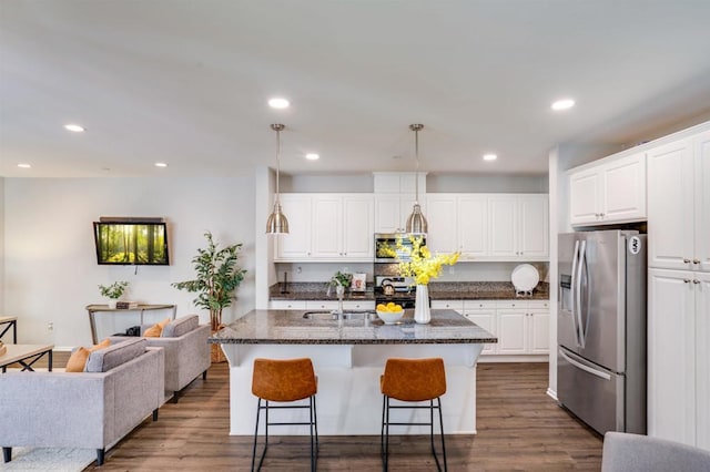 kitchen with stainless steel appliances, white cabinetry, hanging light fixtures, and a center island with sink