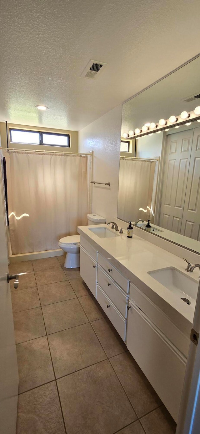 bathroom with a textured ceiling, tile patterned flooring, vanity, and toilet