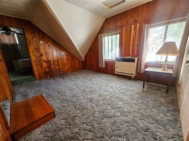 additional living space with heating unit, vaulted ceiling, wood walls, and a healthy amount of sunlight