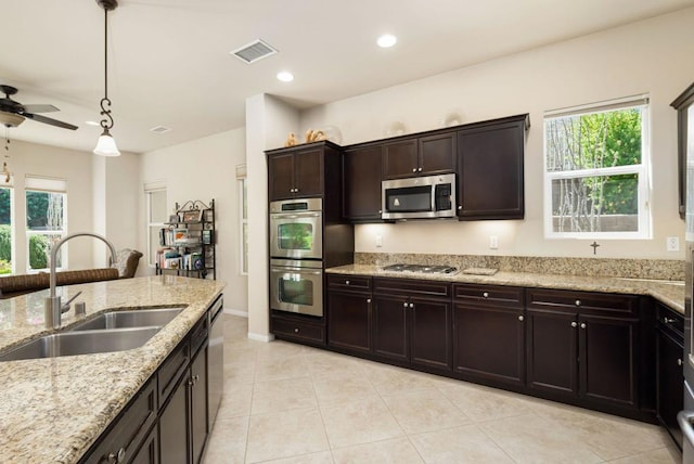 kitchen with light stone counters, hanging light fixtures, appliances with stainless steel finishes, dark brown cabinets, and sink