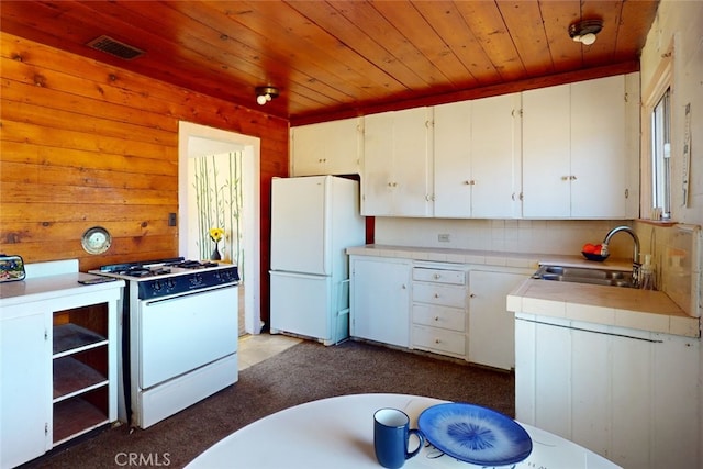 kitchen with white cabinets, sink, white appliances, wooden walls, and light carpet