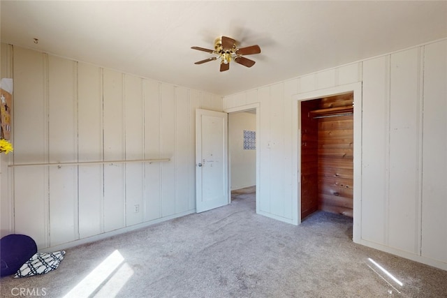 unfurnished bedroom with light carpet, wooden walls, a closet, and ceiling fan