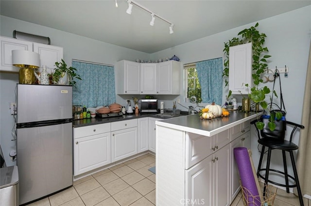 kitchen with light tile patterned flooring, stainless steel fridge, kitchen peninsula, white cabinetry, and a breakfast bar