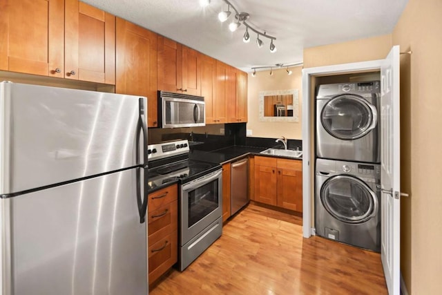 kitchen with stainless steel appliances, light hardwood / wood-style floors, sink, and stacked washer / drying machine