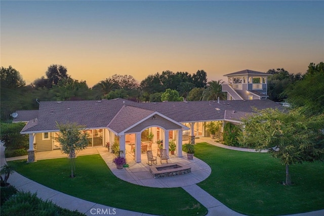 back house at dusk with a patio area and a lawn