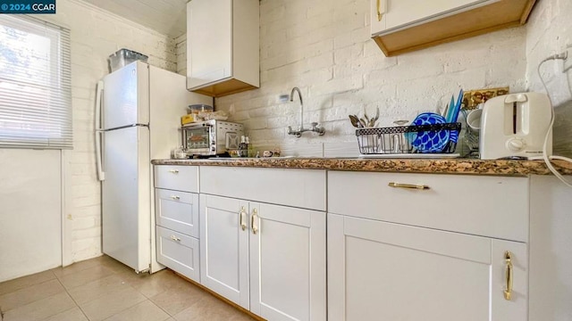 kitchen featuring dark stone countertops, brick wall, white fridge, and white cabinetry