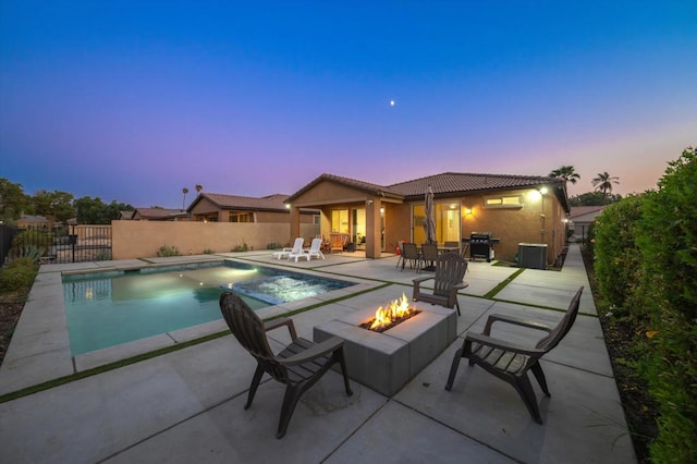 pool at dusk featuring a patio, area for grilling, and a fire pit