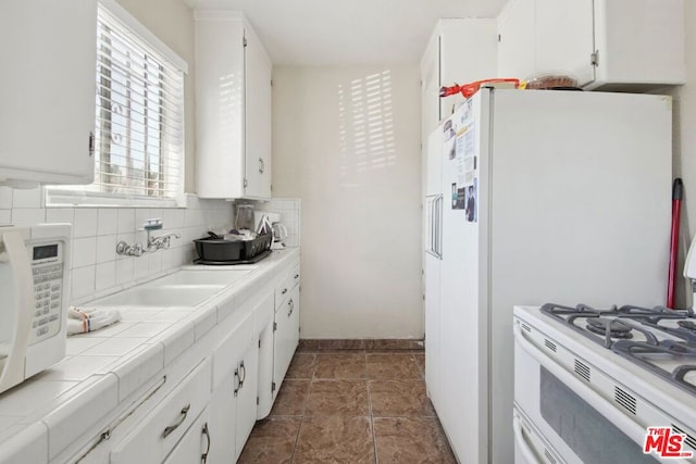 kitchen featuring tile countertops, backsplash, white cabinetry, and sink