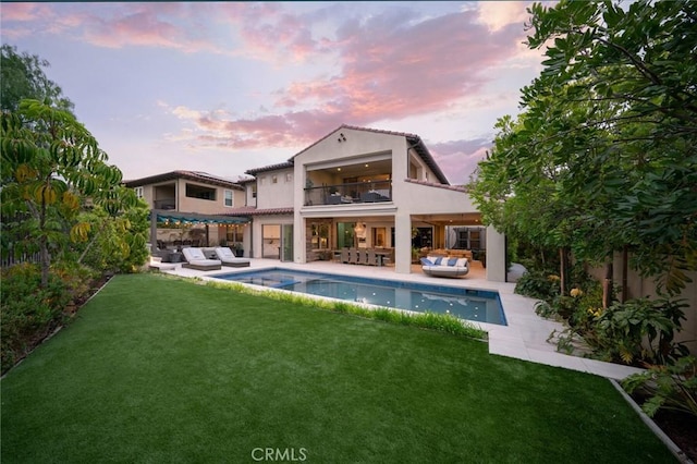 back house at dusk featuring a yard, a patio area, a balcony, and an outdoor hangout area