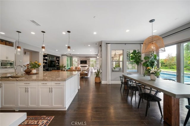 kitchen featuring stainless steel microwave, white cabinetry, sink, and decorative light fixtures