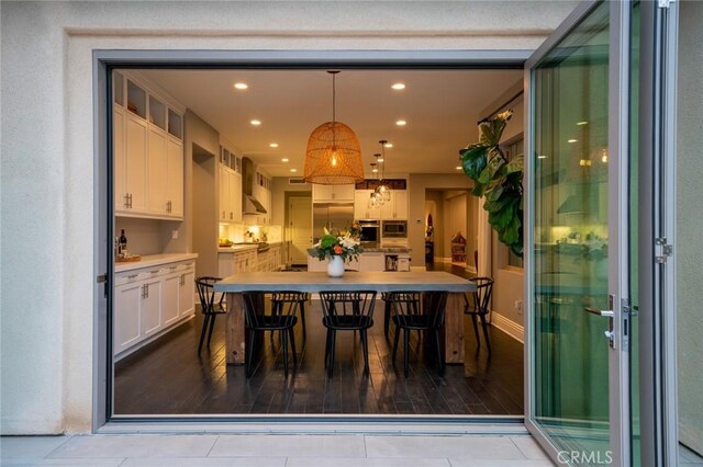 interior space featuring white cabinetry, wall chimney range hood, a kitchen breakfast bar, light hardwood / wood-style floors, and decorative light fixtures