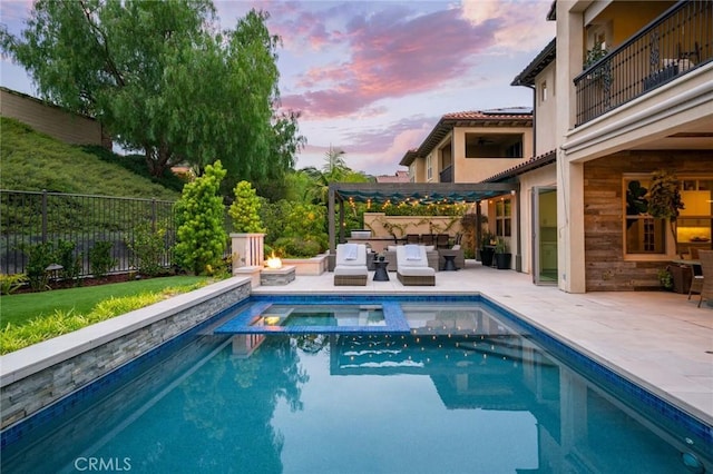 pool at dusk featuring an in ground hot tub, a patio, and an outdoor living space with a fire pit