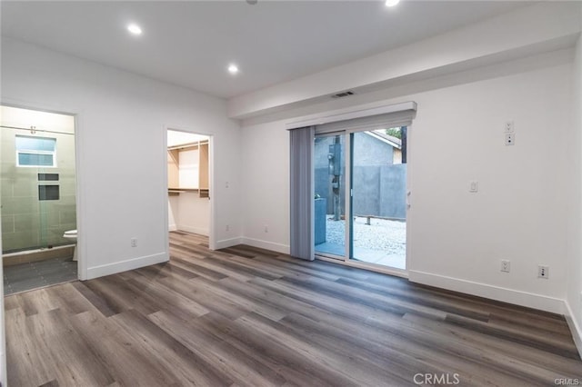 unfurnished bedroom featuring connected bathroom, access to exterior, a spacious closet, dark hardwood / wood-style floors, and a closet