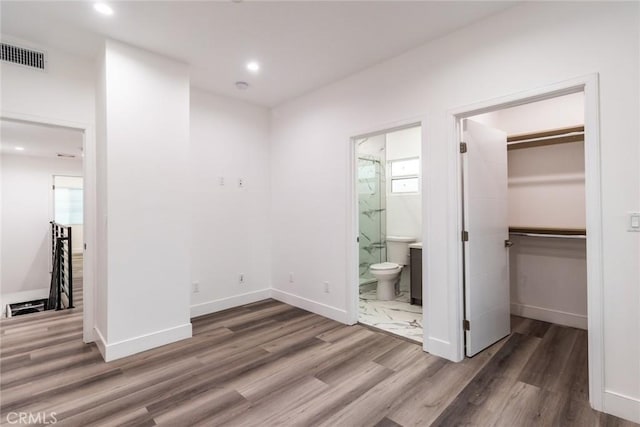 unfurnished bedroom featuring connected bathroom, a spacious closet, a closet, and hardwood / wood-style flooring