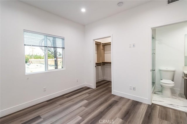 unfurnished bedroom with dark hardwood / wood-style flooring, ensuite bathroom, a spacious closet, and a closet