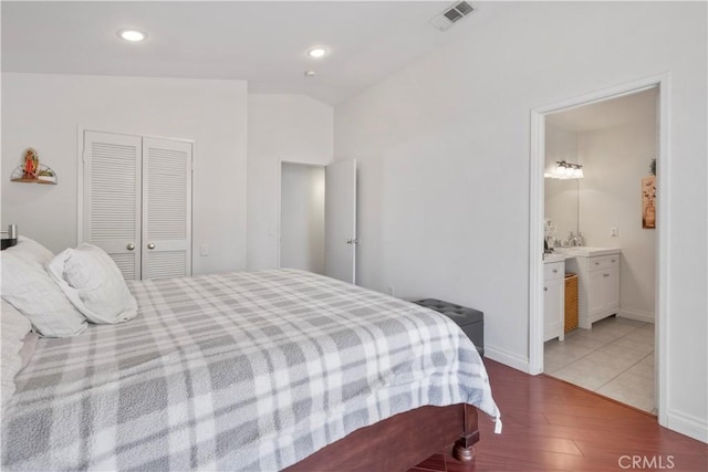 bedroom with vaulted ceiling, a closet, light hardwood / wood-style flooring, and ensuite bath